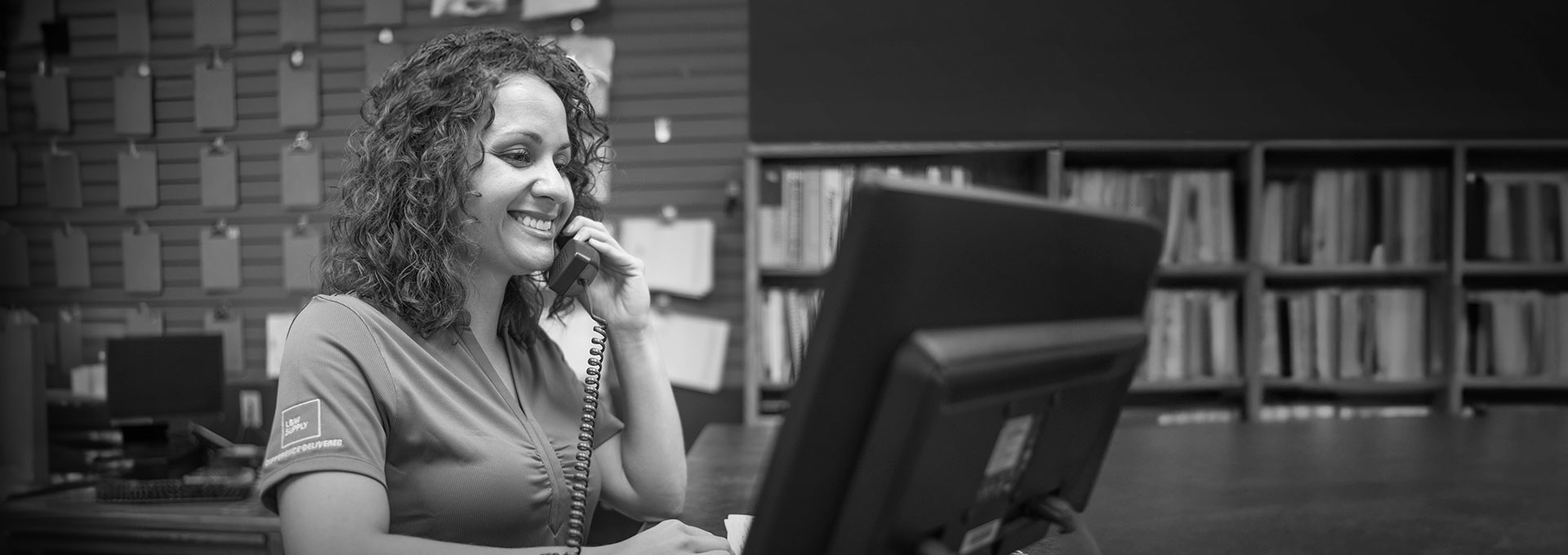 A smiling woman on the phone in front of a computer at a L&W Supply branch location.